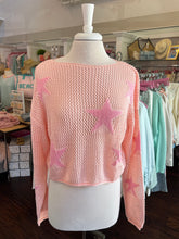 Pink knit sweater with star patterns on a mannequin in a store setting.