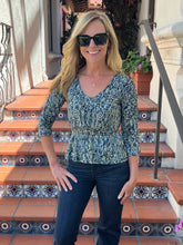 A woman wearing a blue and green patterned peplum top and dark jeans, standing on outdoor tiled steps.