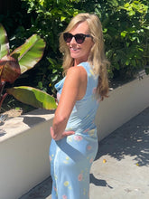 Woman in a light blue floral dress standing outdoors with greenery in the background
