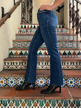 A person wearing blue flare jeans and black heeled ankle boots, standing on patterned terracotta stairs indoors.