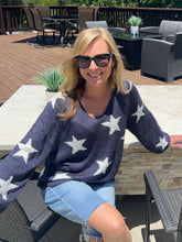Woman wearing a navy sweater with white star patterns and denim shorts, sitting outdoors.