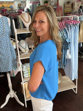 Woman in a blue shirt standing in a clothing store with racks of clothes and mannequins.