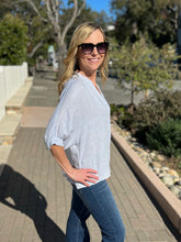 Woman wearing a light blue top and sunglasses outdoors on a sunny day.