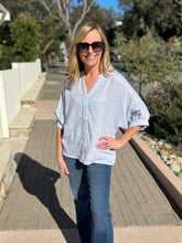 Woman wearing a light blue top and sunglasses outdoors on a sunny day.