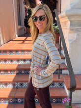 A woman wearing a beige and brown striped long-sleeve knit top and dark brown pants, standing on outdoor terracotta tiled steps.