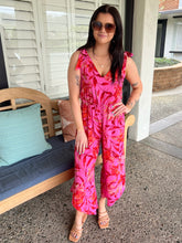 Woman in a pink floral jumpsuit standing on a porch.