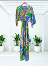 Colorful patterned kimono sleeve maxi dress hanging on a rack with plants in the background