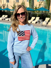 Woman wearing a light blue sweater with an American flag design by a pool.