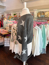 Mannequin wearing a black knit sweater with white star patterns in a store setting.