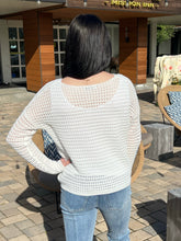 Person wearing a white textured sweater and blue jeans standing outdoors.