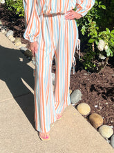 Person wearing a colorful striped outfit standing outdoors on a stone path with greenery.