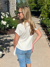 Woman in a white t-shirt and blue jeans standing on a sidewalk with flowers and a building in the background