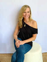 Woman sitting on a white stool wearing a black top and blue jeans against a plain background