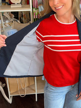 Person wearing a red sweater with white stripes and blue jeans, standing in a store.