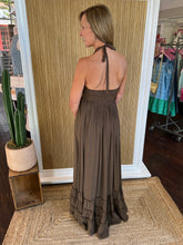Woman wearing a brown halter neck dress in a store setting with a cactus plant and clothing racks in the background.
