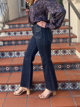 A person wearing dark blue high-waisted flare jeans, a patterned long-sleeve blouse, and beige heeled sandals, standing on terracotta tiled stairs with decorative blue and white mosaic tiles.