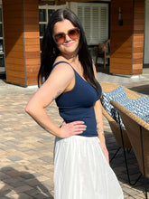 Woman in a navy top and white skirt standing outdoors near a wooden building.