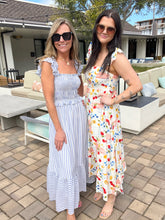 Two women standing outdoors on a patio, wearing sunglasses and long dresses.