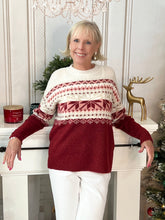 Woman wearing a red jacquard snowflake sweater standing in a festive setting with a reindeer decorated. 