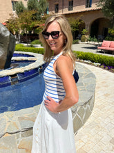 Woman in a striped dress standing by a pool with a building and garden in the background
