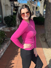 Woman in a fuchsia long-sleeve top and black pants standing outdoors on a sidewalk.