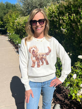 Woman wearing a white sweatshirt with a dog graphic, standing outdoors near greenery.