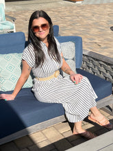 Woman in a striped dress sitting on a blue cushioned chair outdoors.