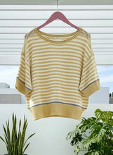 Yellow and white striped sweater on a hanger with plants in the background