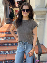 A woman wearing a brown and gray striped ribbed knit top with a drawstring waist and light blue jeans, standing on tiled outdoor steps.