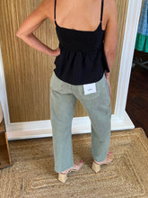 Person wearing light olive barrel jeans and a black top showing back view in a store setting.