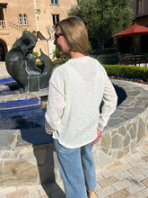 Woman standing by a sculpture in an outdoor setting with a building and trees in the background