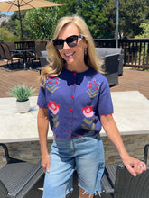 Woman wearing a floral short-sleeve cardigan and sunglasses outdoors.