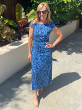 Woman in a blue dress standing outdoors with plants in the background
