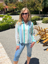 Woman wearing a striped shirt and sunglasses outdoors with greenery in the background