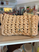 Woven handbag with starfish charm on a wooden surface in a store setting