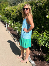 Woman wearing a blue and green dress standing outdoors near a garden.
