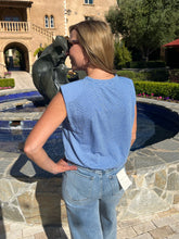 Person in a blue sleeveless top and jeans standing by a fountain with a building in the background