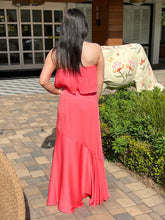 Woman in a coral dress standing on a patio with a garden and house in the background
