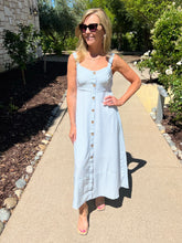 Woman in a light blue striped dress standing on a sidewalk with greenery in the background