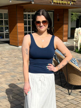 Woman wearing a navy tank top and white skirt standing outdoors in front of a building.
