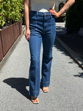 A person wearing high-waisted, wide-leg blue jeans with contrast light stitching, standing outdoors on a paved path.