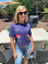 Woman wearing a floral embroidered shirt and sunglasses outdoors on a patio.