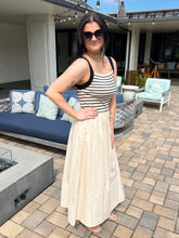 Woman in a striped top and beige skirt standing on a patio with outdoor furniture.