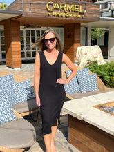 Woman in a black dress standing in front of 'Carmel Mission Inn' with outdoor furniture.