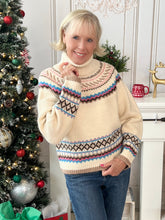 Woman wearing a cream turtle neck sweater with a colorful pattern in a festive setting with a decorated Christmas tree.