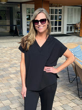 Woman wearing a black outfit standing outdoors on a paved area.