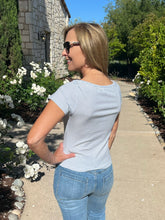 Woman in a striped shirt and jeans standing on a sidewalk with flowers and a building in the background