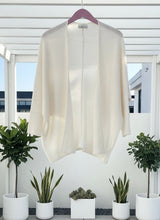 Ivory open cardigan sweater hanging from a pink hanger on a  pergola.