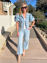 Woman wearing a light blue cropped denim jacket and jeans outdoors on a sunny day.