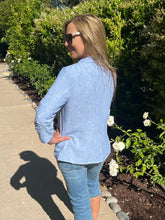 Woman wearing a blue denim jacket and jeans standing outdoors with greenery in the background